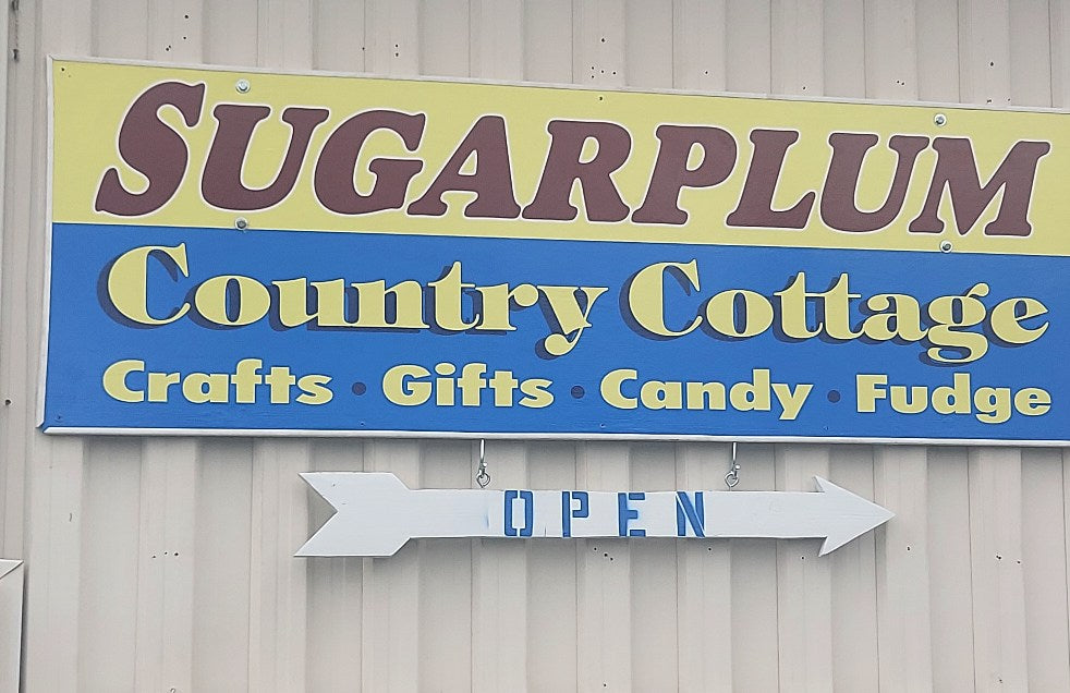 Sign for Sugarplum Country Cottage with text about crafts, gifts, and fudge on a light-colored wall.